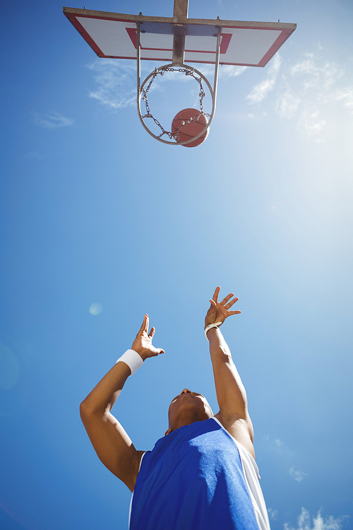 Directly below shot of male teenager playing basketball against sky on sunny day
