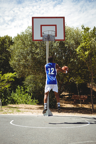 Teenage basketball player scoring while practicing at court against sky