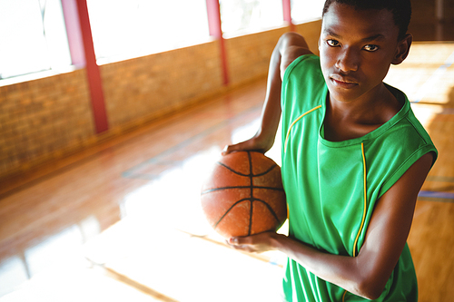 Portrait of teenage boy holding basketball while standing in court