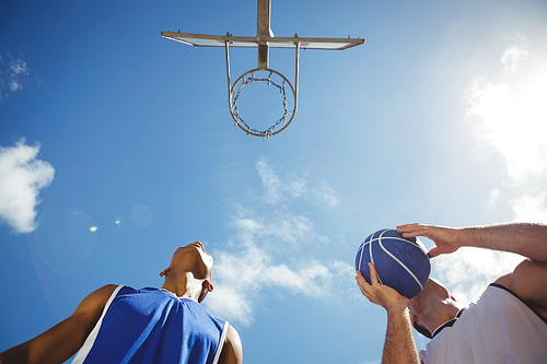 Low angle view basketball players practicing in court against sky on sunny day