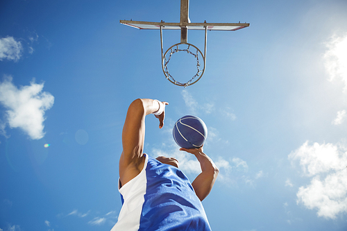 Directly below shot of basketball player taking a shot while playing in court against sky