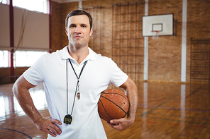 Portrait of confident basketball coach holding ball while standing in court