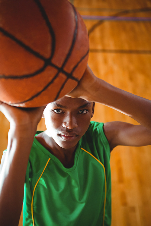 Portrait of teenage boy with basketball standing in court
