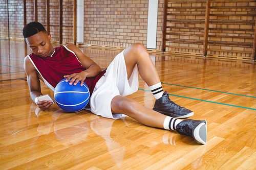 Full length male basketball player using mobile phone while reclining on floor in court