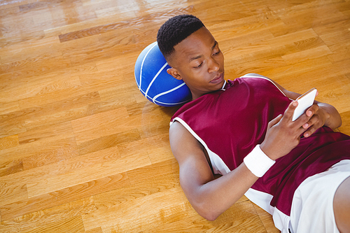 High angle view of male basketball player using mobile phone while lying on floor in court