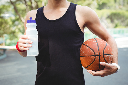 Midsection of  basketball player with holding bottle while standing in court