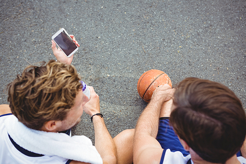 Overhead view of basketball player showing mobile phone to friend while sitting in court