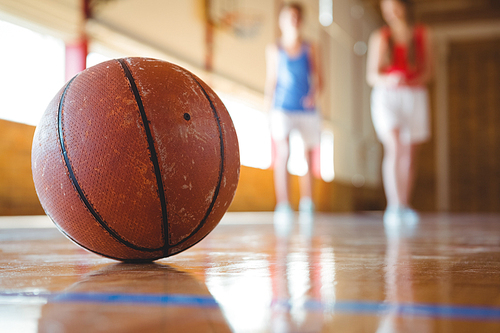 Close up of orange basketball on floor with female players in background