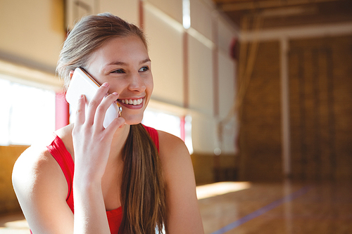 Close up of smiling female basketball player talking on phone while sitting in  court