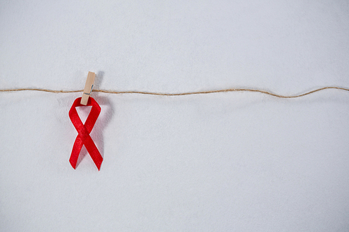 Close-up of red ribbon hanging from clothespin on string against white background
