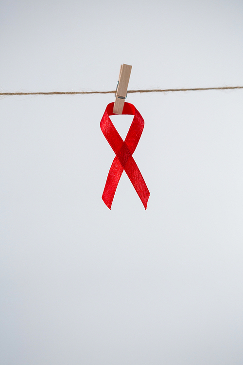 Close-up of red AIDS Awareness ribbon hanging from clothespin on string against white background