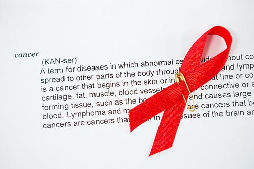 High angle view of red AIDS Awareness ribbon on paper with cancer text