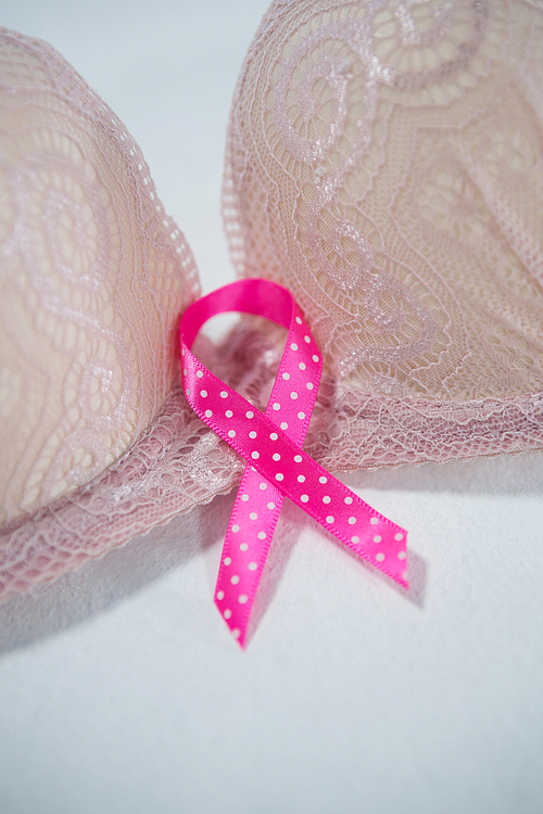 Close-up of spotted pink Breast Cancer Awareness ribbon on bra against white background