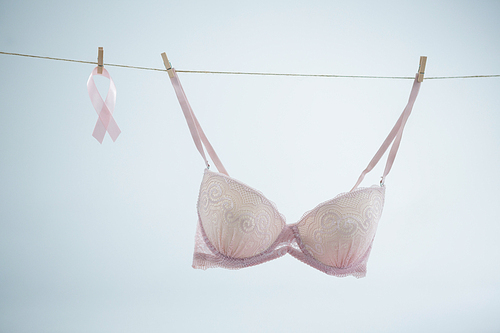 Pink Breast Cancer Awareness ribbon hanging by bra on string against white background