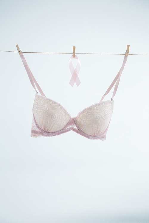 Pink Breast Cancer ribbon hanging by bra on string against white background