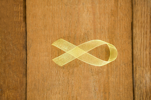 Directly above view of yellow Sarcoma Awareness ribbon on wooden table