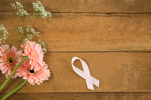 Overhead view of pink Breast Cancer Awareness ribbon by gerbera flowers on wooden table