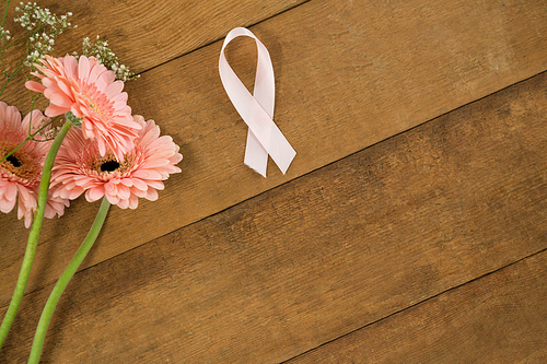 Close-up of pink Breast Cancer Awareness ribbon by gerbera flowers on wooden table