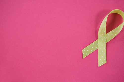 Overhead view of spotted green Lymphoma Awareness ribbon on pink background