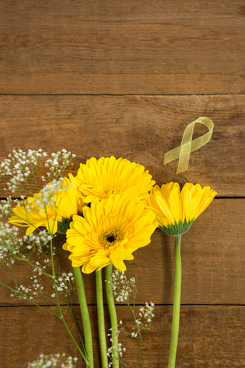 Overhead view of yellow Sarcoma Awareness ribbon by flowers on wooden table