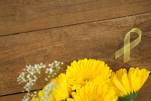 Directly above view of yellow Sarcoma Awareness ribbon by flowers on wooden table