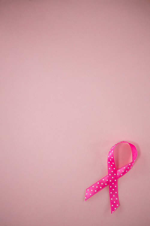 Overhead view of spotted Breast Cancer Awareness ribbon on pink background