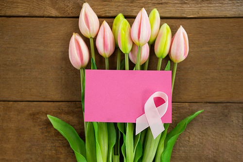 Overhead view of pink Breast Cancer Awareness ribbon with blank card on tulips over wooden table