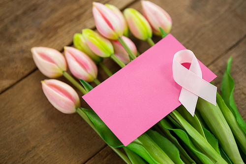 High angle view of pink Breast Cancer Awareness ribbon with blank card on tulips over wooden table