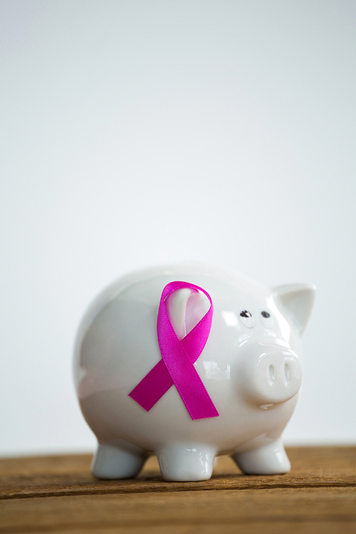 Pink Breast Cancer Awareness ribbon on piggybank over wooden table against white background