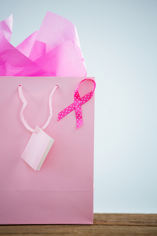 Close-up of pink spotted Breast Cancer Awareness ribbon on shopping bag against white background