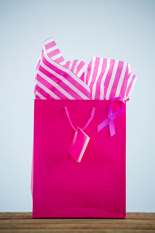 Close-up of vibrant pink Breast Cancer Awareness ribbon on shopping bag against white background