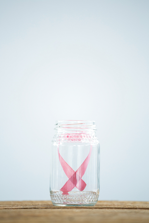 Close-up of pink Breast Cancer Awareness ribbon in glass jar on table against white background