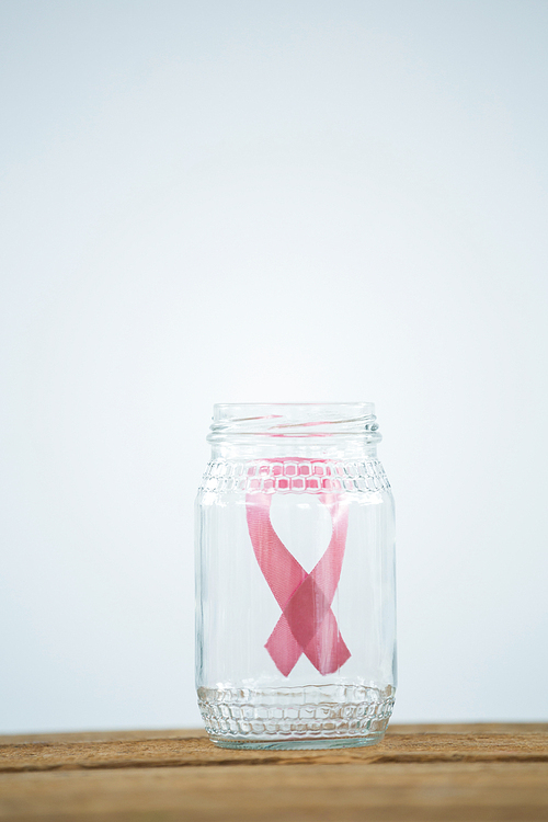 Pink Breast Cancer Awareness ribbon in glass jar on piggybank on wooden table against white background