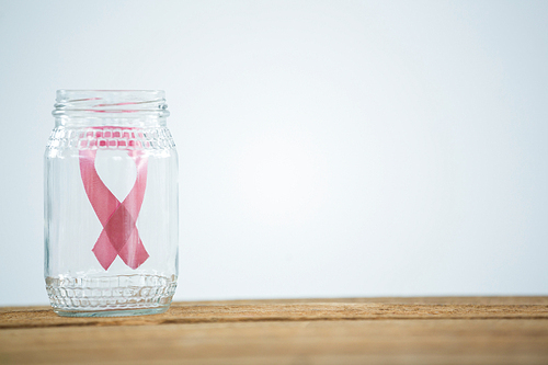Close-up of pink Breast Cancer Awareness ribbon in glass jar on piggybank against white background