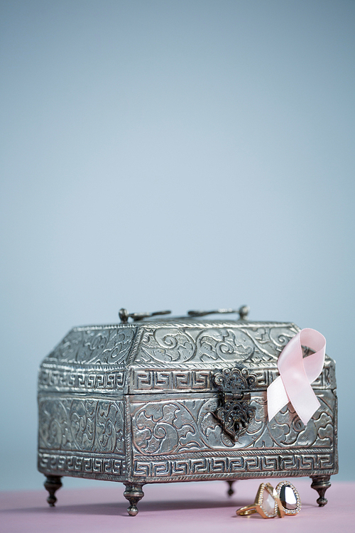 Close-up of pink Breast Cancer Awareness ribbon with chest and rings on table against white background