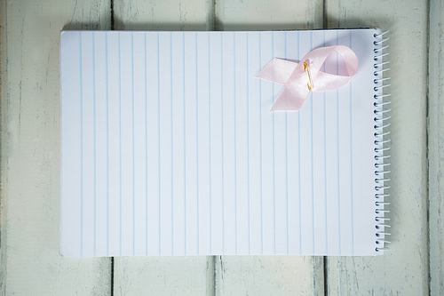 Overhead view of pink Breast Cancer Awareness ribbon and spiral notepad on wooden table