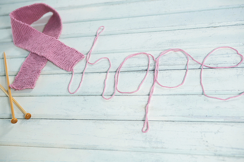 High angle view of pink Breast Cancer Awareness ribbon by hope text and crochet needles on white wooden table