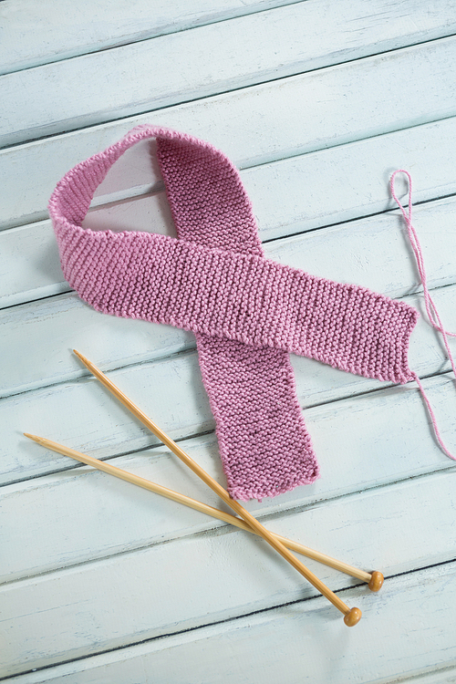 High angle view of pink woolen Breast Cancer Awareness ribbon by crochet needles on white wooden table