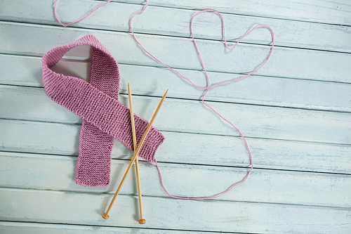 High angle view of pink woolen Breast Cancer Awareness ribbon by crochet needles with heart shape on white wooden table