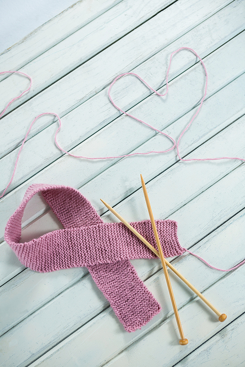 High angle view of pink Breast Cancer Awareness ribbon by crochet needles with heart shape on white wooden table