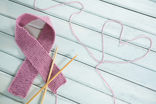 Close-up of pink Breast Cancer Awareness ribbon by crochet needles with heart shape on white wooden table