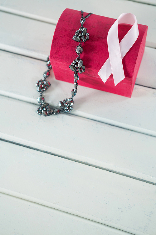 High angle view of pink Breast Cancer Awareness ribbon and jewelry with red box on white wooden table