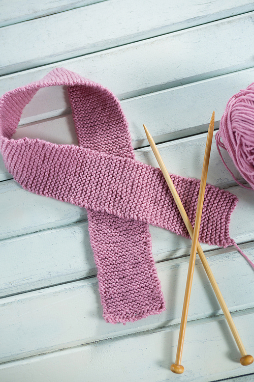 Close-up of pink woolen Breast Cancer Awareness ribbon with crochet needles on wooden table