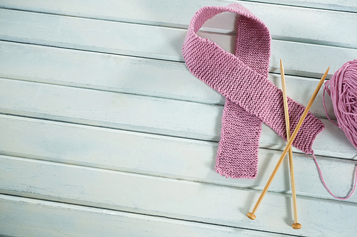 Overhead view of pink woolen Breast Cancer Awareness ribbon with crochet needles on wooden table