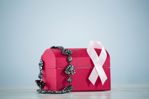 Close-up of jewelry with red box and pink Breast Cancer Awareness ribbon against gray background