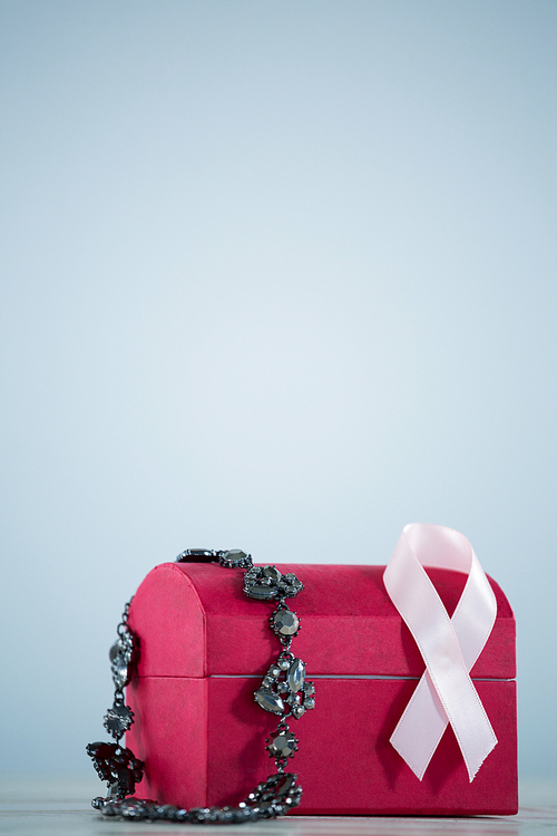 Close-up of pink Breast Cancer Awareness ribbon and jewelry on red box against gray background
