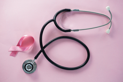 Overhead view of stethoscope by Breast Cancer Awareness ribbon on pink background
