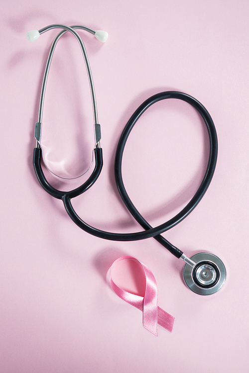 Directly above view of stethoscope by Breast Cancer Awareness ribbon on pink background