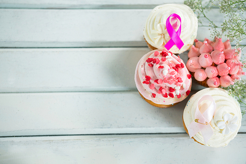 Overhead view of Breast Cancer Awareness pink ribbons on cupcakes over white wooden table