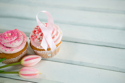 High angle view of Breast Cancer Awareness pink ribbons on cupcakes with tulips over white wooden table